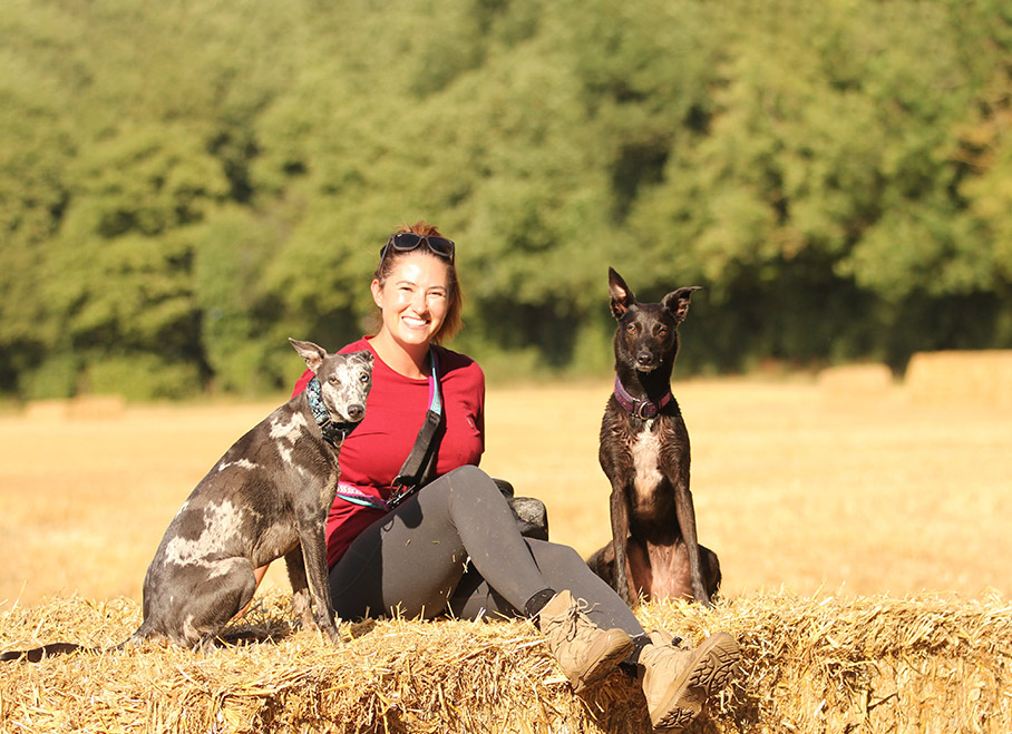Jo sitting on a hay bale with two dogs