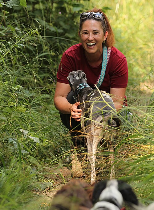 Jo crouching in long grass greeting a dog